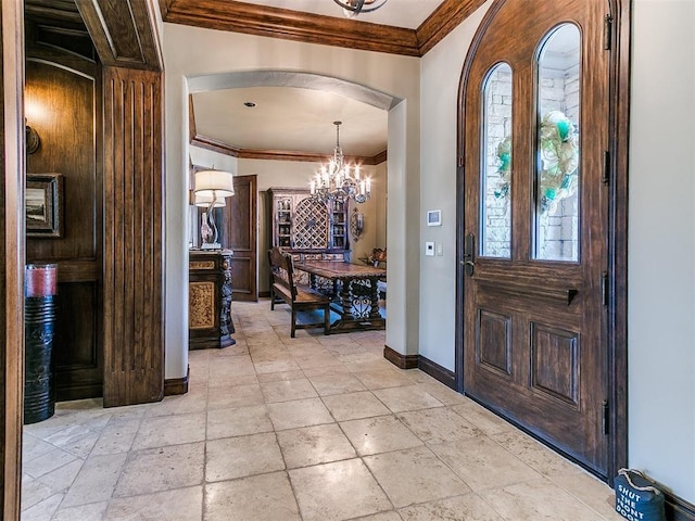 entryway with arched walkways, stone tile flooring, an inviting chandelier, ornamental molding, and baseboards