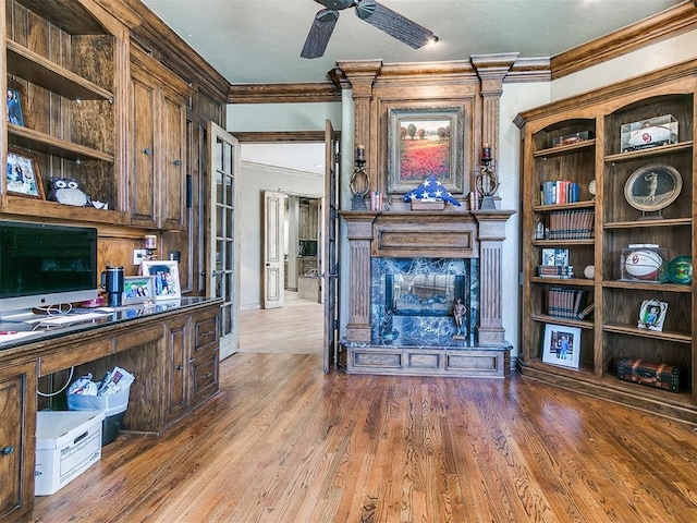 unfurnished office featuring a fireplace, wood finished floors, a ceiling fan, and crown molding