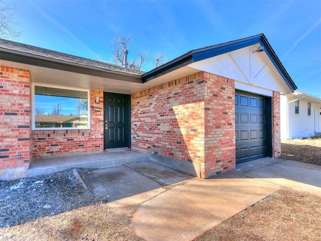 view of exterior entry featuring brick siding, driveway, and an attached garage