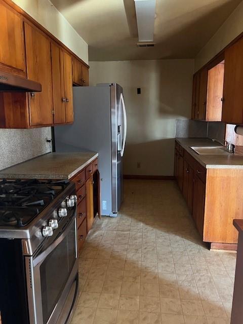 kitchen with appliances with stainless steel finishes, brown cabinets, a sink, light floors, and backsplash