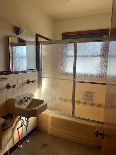 bathroom featuring shower / bath combination with glass door, tile walls, and a sink