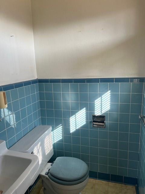 bathroom featuring tile walls, toilet, a wainscoted wall, tile patterned flooring, and a sink