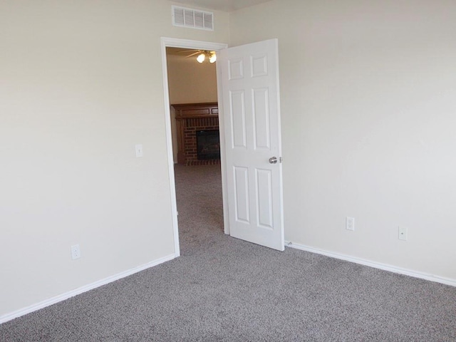 carpeted spare room featuring a brick fireplace, baseboards, and visible vents