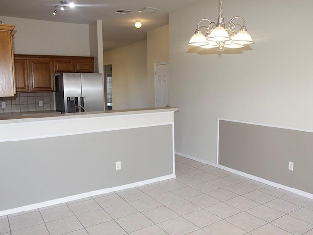 kitchen featuring light tile patterned floors, hanging light fixtures, backsplash, brown cabinetry, and stainless steel fridge