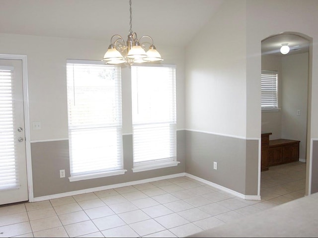 unfurnished dining area with light tile patterned floors, baseboards, arched walkways, vaulted ceiling, and a notable chandelier