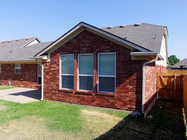 rear view of house with a shingled roof, a lawn, fence, a patio area, and brick siding