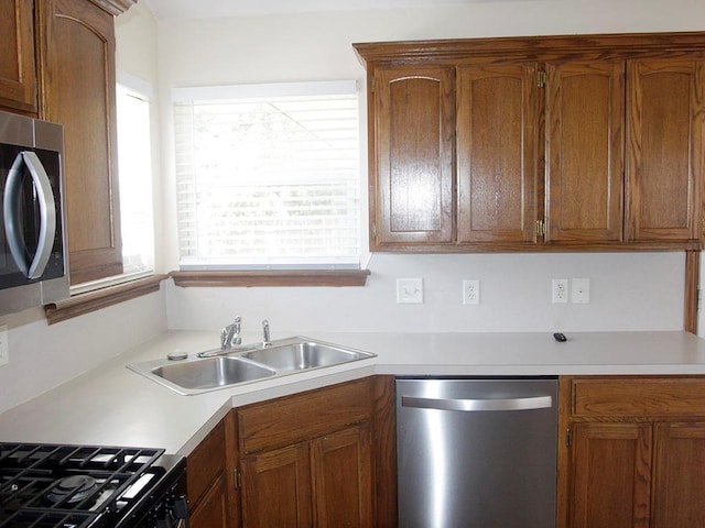 kitchen featuring brown cabinets, appliances with stainless steel finishes, light countertops, and a sink