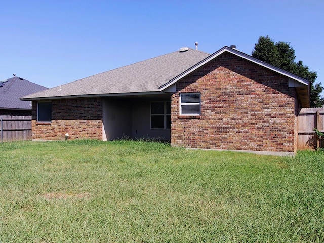 back of house featuring a yard, roof with shingles, fence, and brick siding