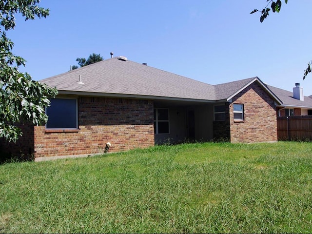 rear view of house featuring brick siding, a lawn, fence, and roof with shingles