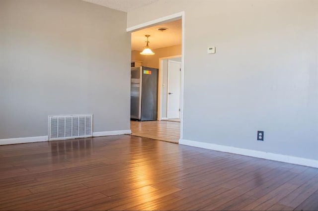 spare room featuring wood finished floors, visible vents, and baseboards