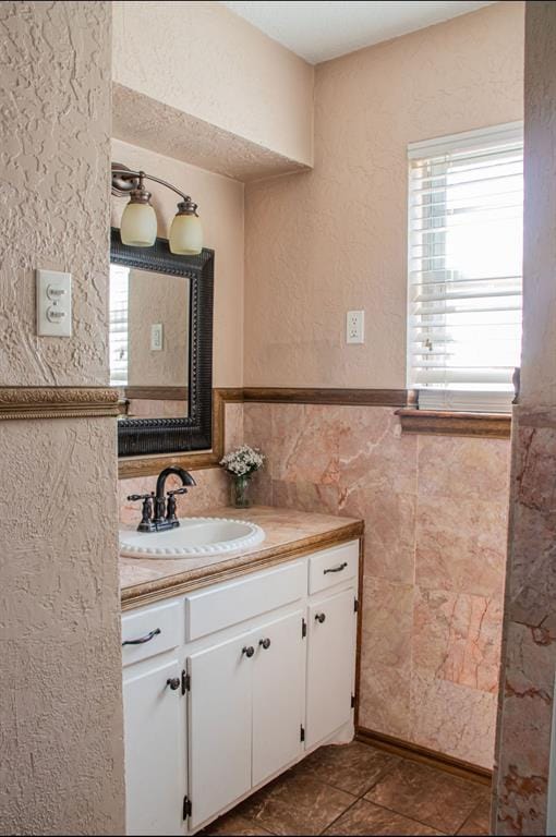 bathroom with a textured wall, wainscoting, tile walls, and vanity