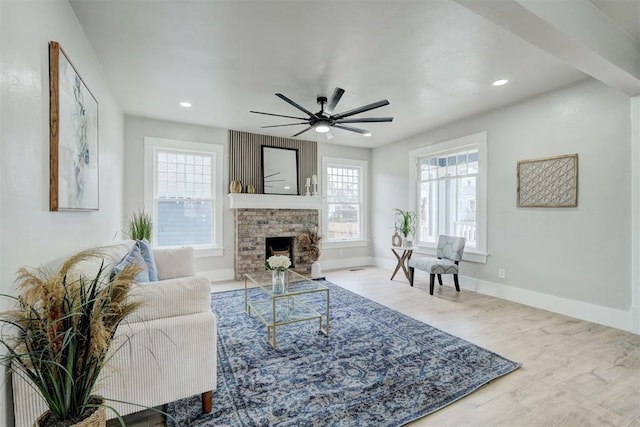 living area with a ceiling fan, a fireplace with flush hearth, baseboards, and wood finished floors