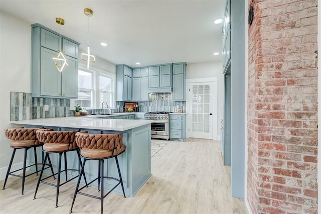 kitchen featuring a peninsula, a sink, high end stainless steel range oven, light wood finished floors, and tasteful backsplash