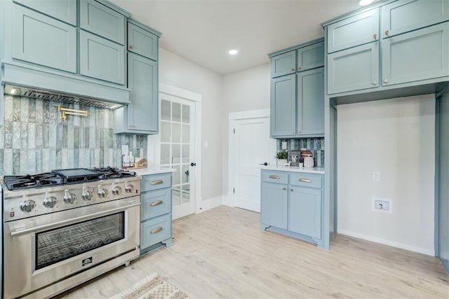 kitchen with tasteful backsplash, high end stainless steel range, custom exhaust hood, light countertops, and light wood-type flooring