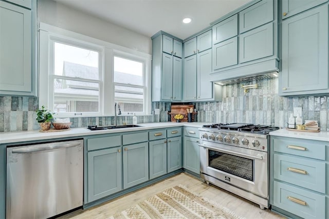 kitchen featuring tasteful backsplash, appliances with stainless steel finishes, light countertops, light wood-type flooring, and a sink