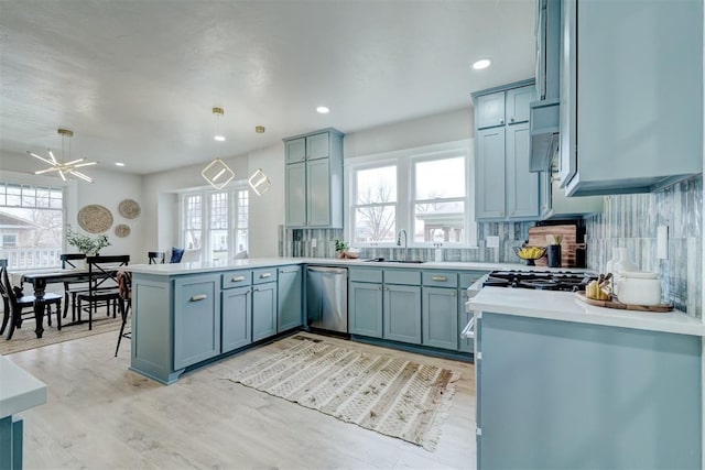 kitchen featuring tasteful backsplash, dishwasher, a peninsula, light countertops, and a sink