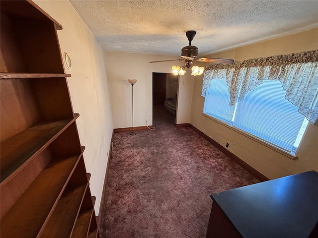 unfurnished dining area with a textured ceiling, dark carpet, a ceiling fan, and baseboards