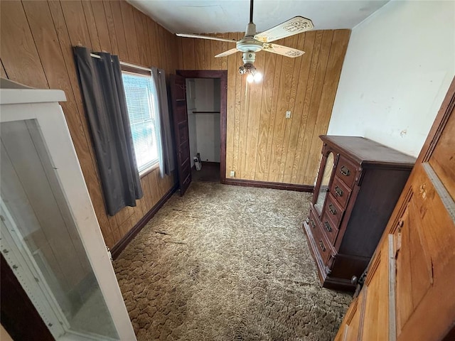 interior space with a ceiling fan, carpet, wooden walls, and baseboards