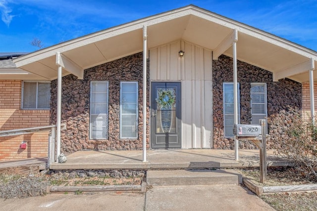 view of exterior entry featuring board and batten siding, covered porch, and brick siding