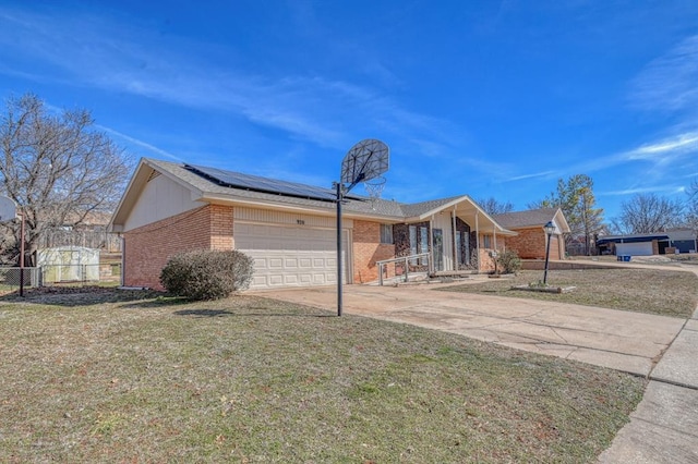 ranch-style home with concrete driveway, an attached garage, fence, roof mounted solar panels, and brick siding