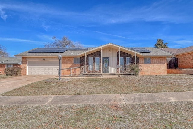 view of front facade with a garage, roof mounted solar panels, brick siding, and driveway