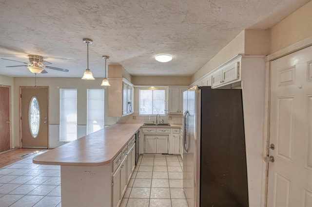 kitchen featuring light tile patterned floors, a peninsula, a sink, appliances with stainless steel finishes, and backsplash