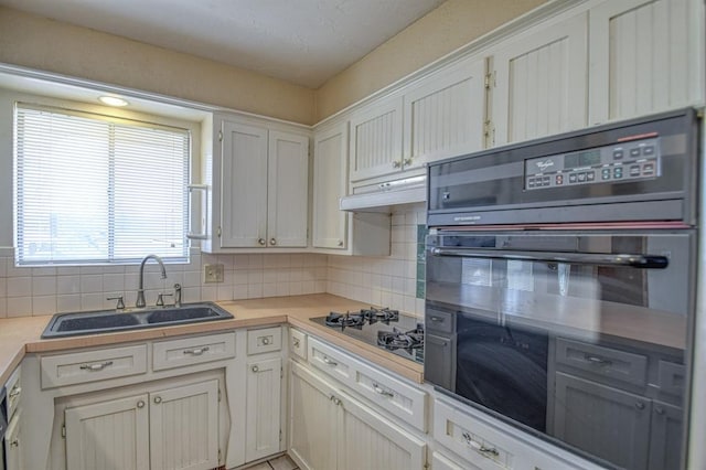 kitchen featuring light countertops, a sink, white cabinetry, and under cabinet range hood