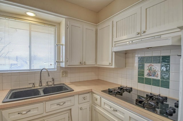 kitchen with light countertops, a sink, under cabinet range hood, and black gas stovetop