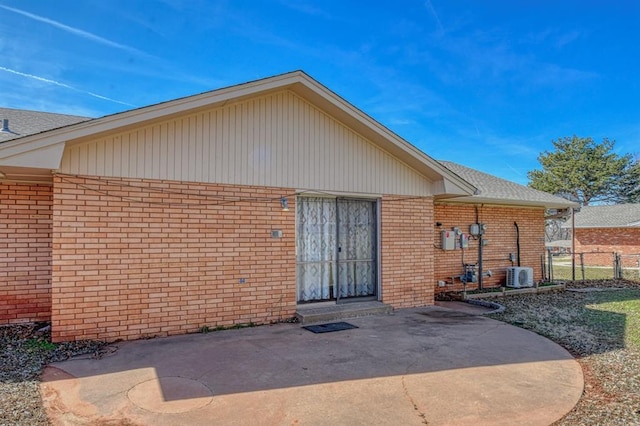 rear view of property featuring a shingled roof, a patio, fence, central AC, and brick siding