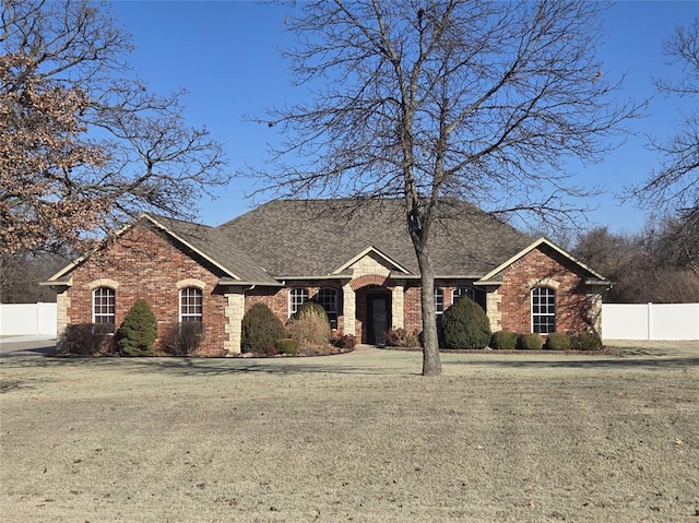 french provincial home with a shingled roof, brick siding, fence, and a front lawn