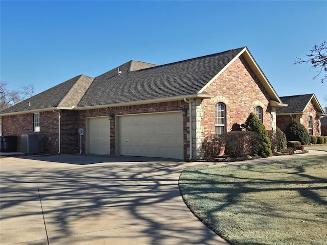 view of property exterior with a garage, driveway, roof with shingles, central AC, and brick siding