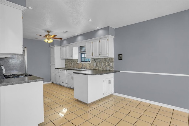 kitchen featuring tasteful backsplash, dark countertops, white cabinets, and white dishwasher