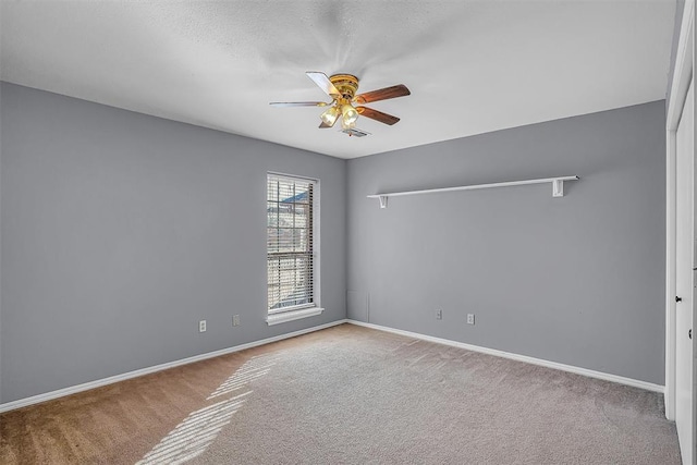 empty room with carpet, a ceiling fan, and baseboards