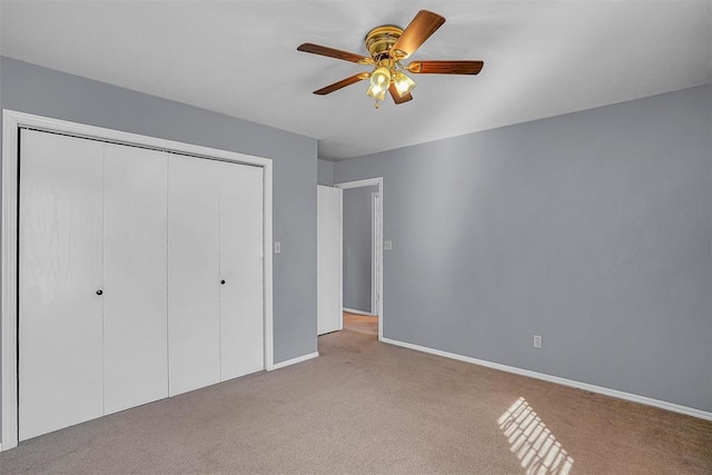 unfurnished bedroom with a closet, light carpet, ceiling fan, and baseboards