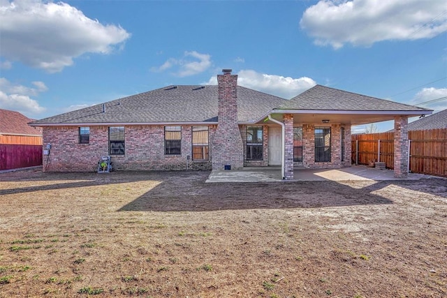 rear view of property with a patio, a fenced backyard, brick siding, roof with shingles, and a chimney