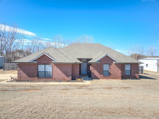 ranch-style home with brick siding, a front lawn, and roof with shingles