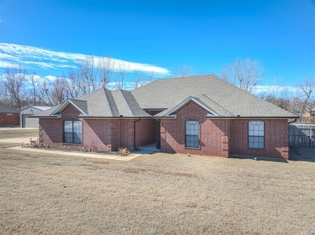 single story home featuring brick siding, roof with shingles, a front lawn, and fence