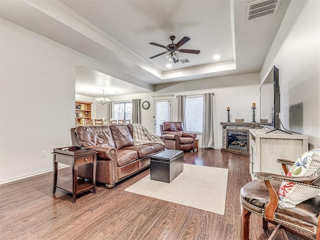 living room featuring ornamental molding, a tray ceiling, dark wood finished floors, and visible vents