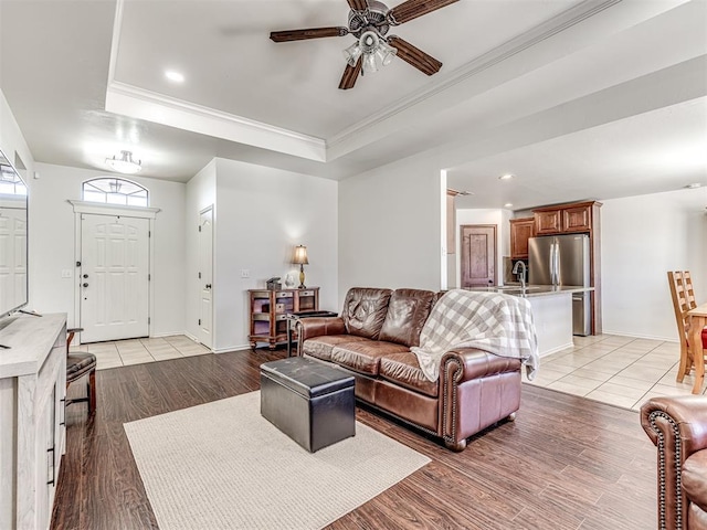 living area featuring baseboards, light wood-style flooring, a tray ceiling, and crown molding