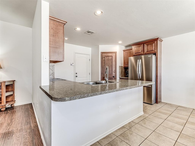 kitchen featuring recessed lighting, visible vents, freestanding refrigerator, a sink, and a peninsula