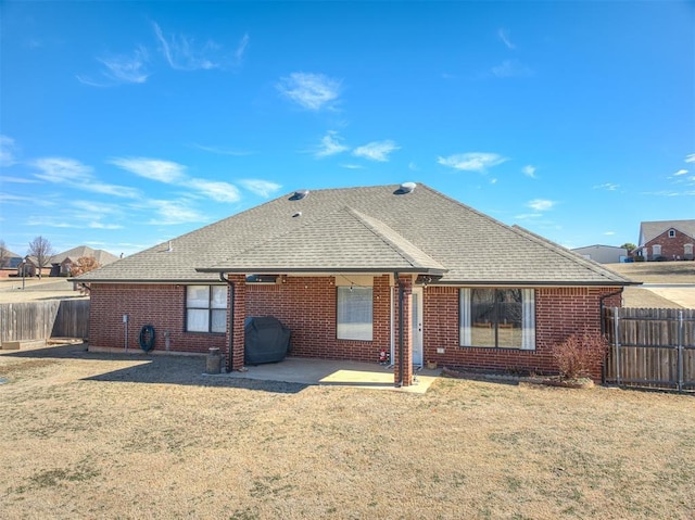 back of house featuring a patio area, roof with shingles, brick siding, and a yard