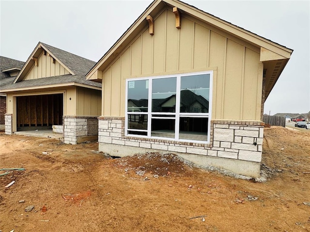 view of front of home with stone siding, board and batten siding, an attached garage, and roof with shingles