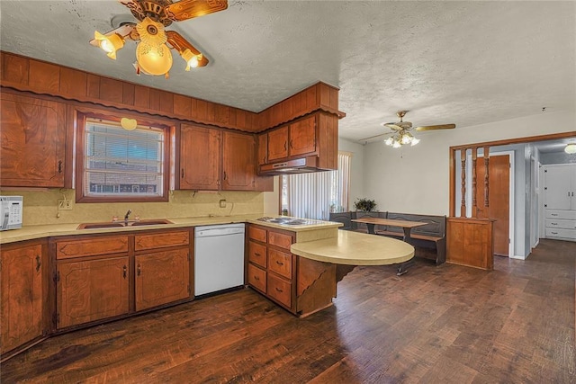 kitchen featuring white appliances, a peninsula, light countertops, under cabinet range hood, and a sink