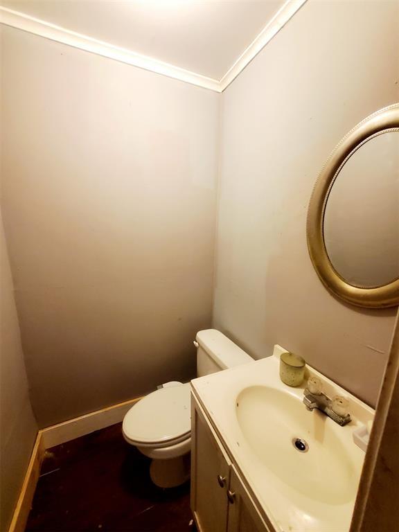 half bathroom with baseboards, toilet, ornamental molding, wood finished floors, and vanity