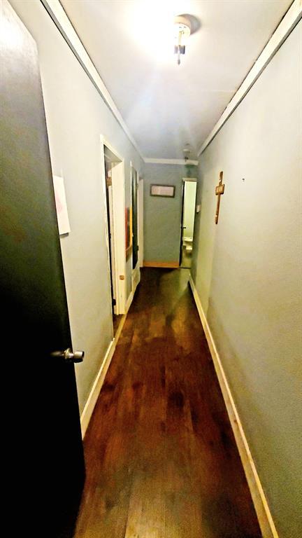 corridor featuring dark wood-style floors, baseboards, and crown molding