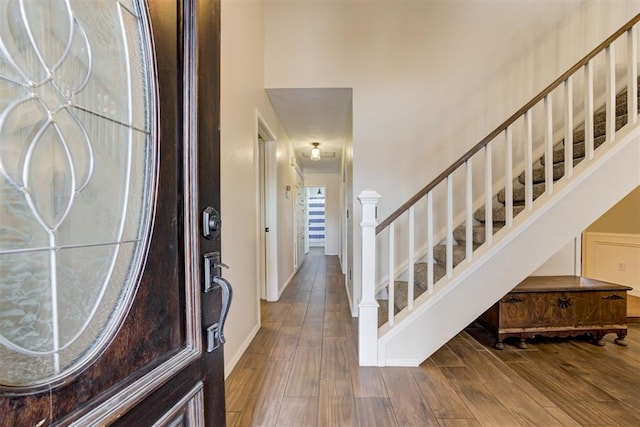 foyer entrance with stairs, wood finished floors, a towering ceiling, and baseboards