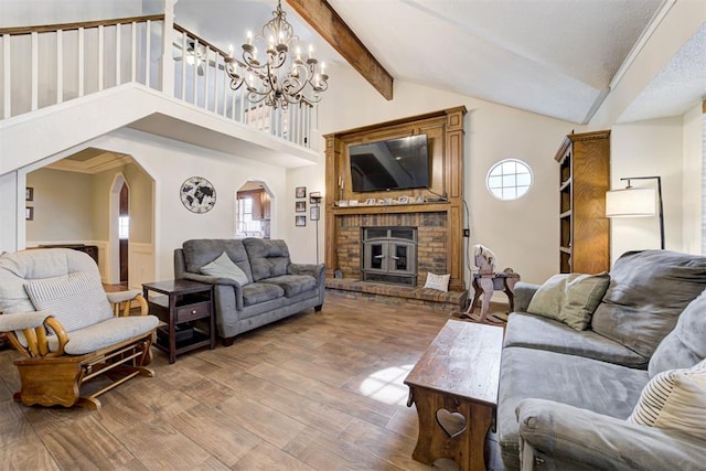 living area with arched walkways, beam ceiling, a brick fireplace, wood finished floors, and high vaulted ceiling