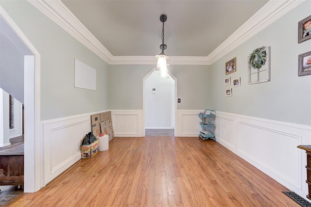 unfurnished dining area featuring light wood finished floors, crown molding, and a wainscoted wall