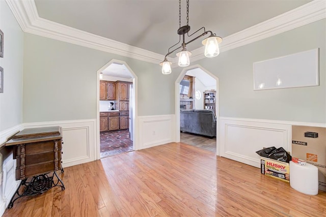 dining room featuring light wood-type flooring, arched walkways, a wainscoted wall, and ornamental molding