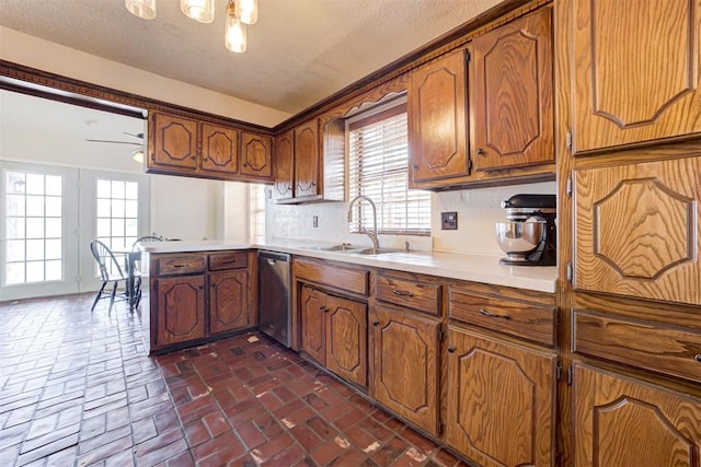 kitchen with brick floor, light countertops, brown cabinetry, a sink, and dishwasher